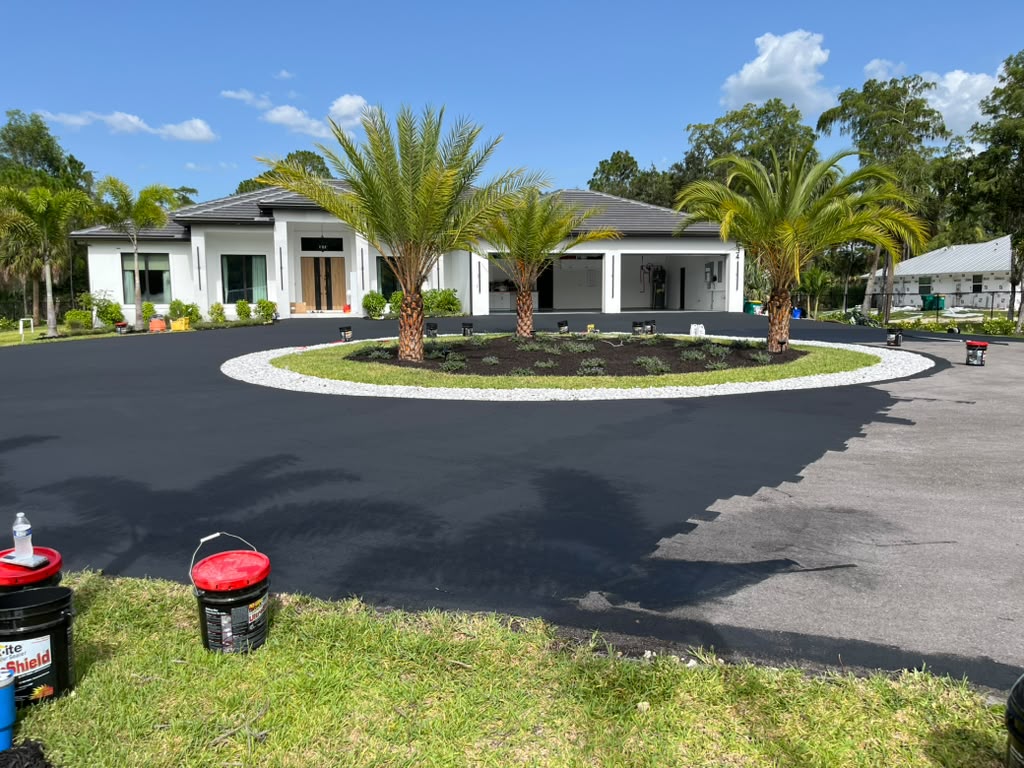 Resurfaced circular driveway restored to a deep, even black finish around a landscaped island in Southwest Florida