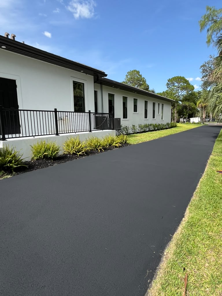Restored asphalt driveway with a rich, uniform dark finish alongside a white Naples-area home