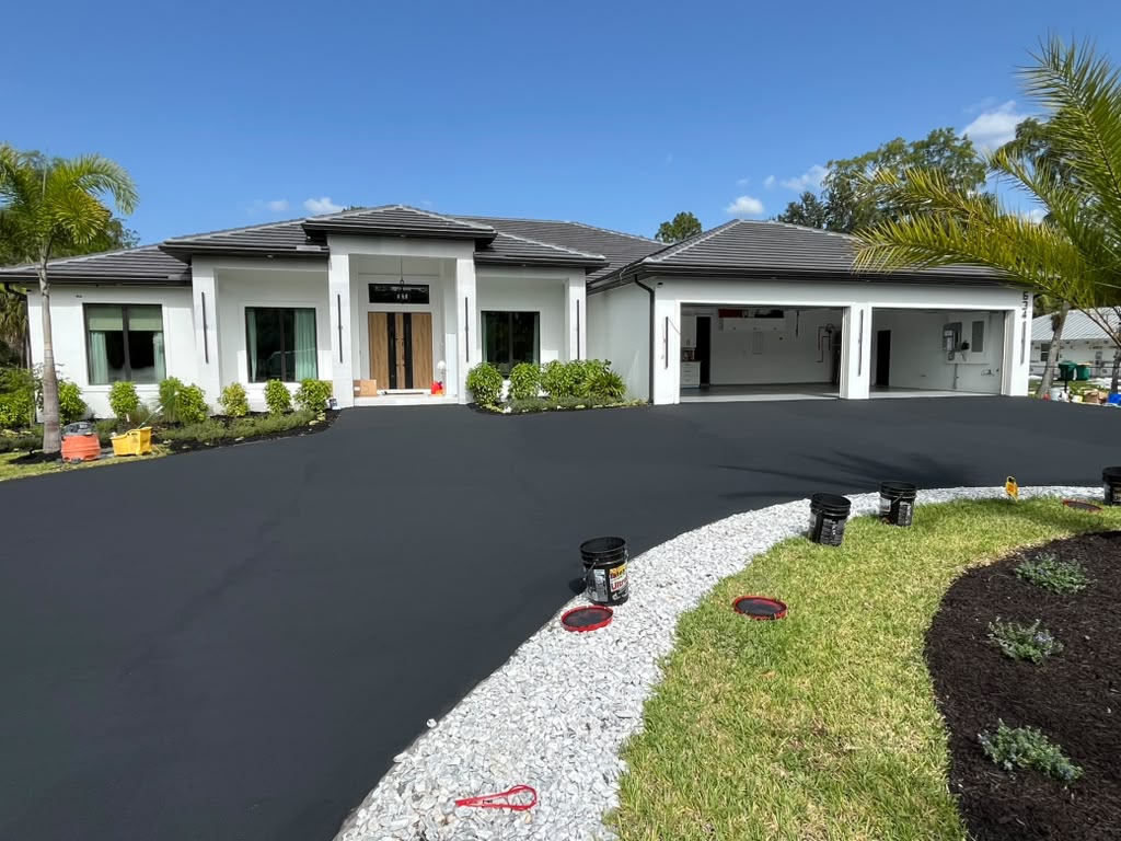 Faded driveway resurfaced back to a dark, protected finish, bordered by white gravel and mulch beds
