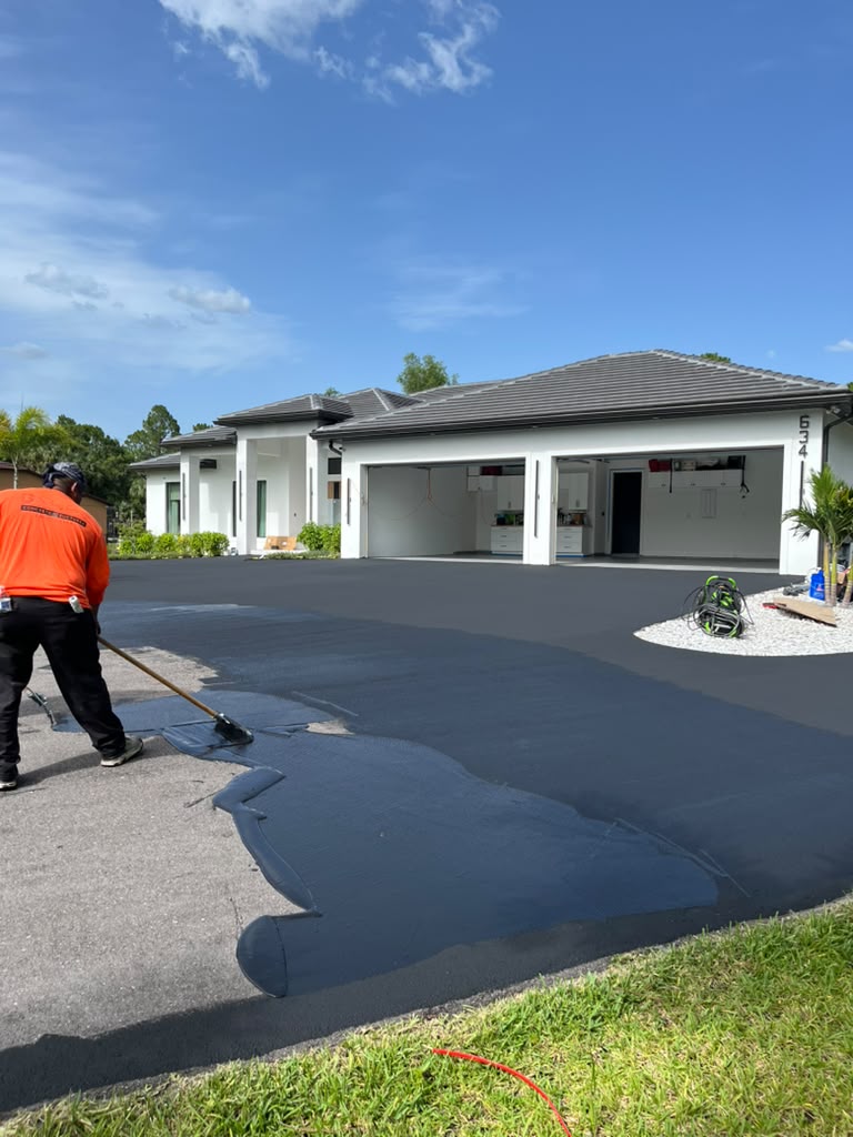 Crew applying a fresh sealcoat wear layer to a driveway in Southwest Florida to restore a dark, uniform asphalt finish